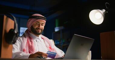 Happy arab man doing internet shopping on computer, spending money on frivolous things. Smiling Middle Eastern person adding payment method on website in order to purchase products photo
