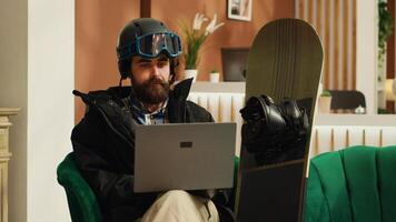 Person checks webpage on laptop before going down on mountain slopes, travelling for skiing activity, searching for winter sport fans reviews. Guest wearing protective helmet. Handheld shot. photo