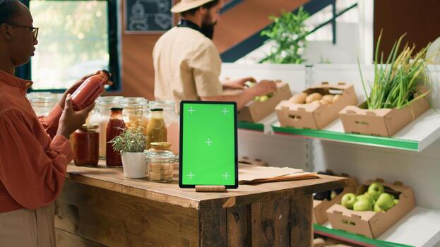 Greenscreen on tablet near client checking bulk products stored in reusable jars, customers supporting nonpolluting lifestyle in local supermarket. Isolated chromakey template on mobile device. photo
