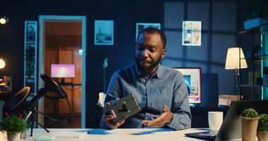 BIPOC content creator filming technology review of newly launched V mount battery, unpacking it and presenting specifications to audience. Internet star showing charging device to viewership photo