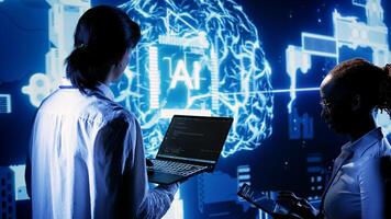 IT team members programming scripts on laptop, employing AI machine learning. African american developer and asian coworker manipulating lines of code for artificial intelligence applications photo