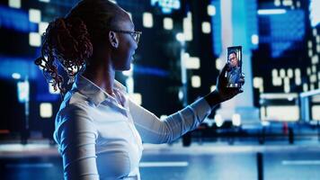 African american woman talking with boyfriend in internet videocall while wandering around dimly illuminated empty city streets at night, needing company to feel safe while walking alone photo
