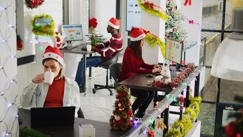 Zoom in portrait shot of happy asian employee working on christmas season in decorated office. Smiling worker solving tasks at desk in diverse xmas ornate workplace next to BIPOC colleagues photo