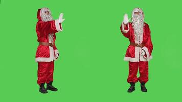 Christmas embodiment character shows palm as stop sign, rejecting ideas and acting displeased over full body greenscreen. Santa claus doing no symbol to refuse something, disapproval. photo