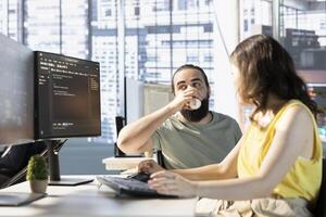 Man with paraplegia drinking coffee, checking colleague doing code review to fix bugs in software. Woman debugging and optimizing code using AI, supervised by manager in wheelchair enjoying beverage photo