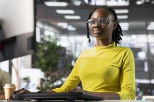 Woman checking paperwork details on PC screen, solving tasks. African american bookkeeper in office making sure documents are compliant with quality assurance expectations and standards photo