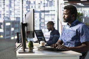 Focused employee analyzing datasets, comparing marketing graphs and checking accounting figures on computer. African american worker solving tasks for team project at workplace photo