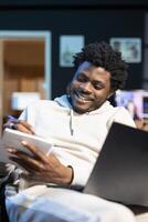 Joyous freelancer working from home, writing down company ideas while watching online . Man excited after coming up with startup conception, using pen to note strategy plan photo
