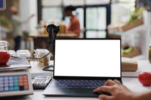 Checkout cashier is using a laptop that has a blank white screen. The vendor is using a minicomputer to view an isolated copyspace template while working at the local organic supermarket. photo