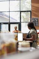 A white-screened tablet has been set on the counter to offer vendors space to advertise eco-friendly products. Digital device at a sustainable store showing an isolated chromakey mockup template. photo