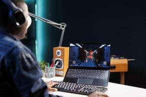 Focused African American player enjoys competitive gaming on digital laptop. Wireless computer, headset, and digital graphics enhances excitement of black woman while playing a game. photo