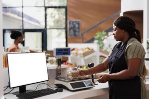 While computer shows an isolated chromakey template for bio food store advertisement, seller weighs organic ethical goods on electronic scale. Desktop pc at counter displaying blank white screen. photo