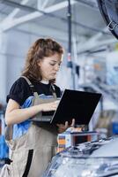 Serviceman in car service orders new engine for damaged vehicle using laptop. Hardworking engineer looking online for components to replace old ones in malfunctioning automobile photo