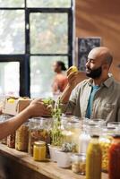 Photo focus on young man in a bio-food store examining fresh farm-grown lemon. Customer of middle eastern ethnicity admiring organic produce in the eco-friendly local market.