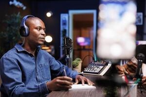 African American influencer in studio, utilizing a high tech microphone for an internet program on livestreaming channel. Man having a podcasting session using professional streaming sound equipment, photo