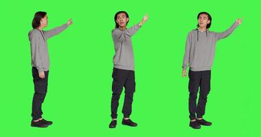 Person indicating left or right directions on camera, pointing to both sides and recommending another path. Asian friendly man advising people to go this way using index fingers, greenscreen. photo