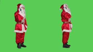 Santa talks on phone call in studio, using smartphone line to have remote chat during christmas holiday. Saint nick cosplay in costume discussing with people against full body greenscreen backdrop. photo