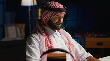 Smilling arab man doing online shopping, using computer to look up tech products to buy. Middle Eastern person adding credit card payment method on secure website, ordering with instant delivery photo