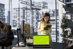 Green screen laptop in front of admin doing software quality assurance, checking source code on tablet. Chroma key notebook in office with woman at work inspecting coding on device photo