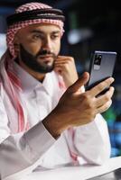 Close-up shot of Middle Eastern male adult holding his cell phone for a conference call. Detailed view of a youthful Muslim man surfing the net on his digital mobile device. photo