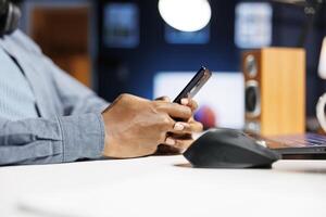 Person sending text messages on mobile phone app, working from home and attending webinar class. Young man freelancer checking social media and listening to online e learning course. Close up. photo