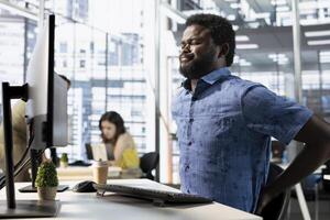 Worker suffering backache from incorrect posture, working with machine learning tech advancing AI. Tired IT expert feeling muscle strain, stretching, transforming data into predictive models photo