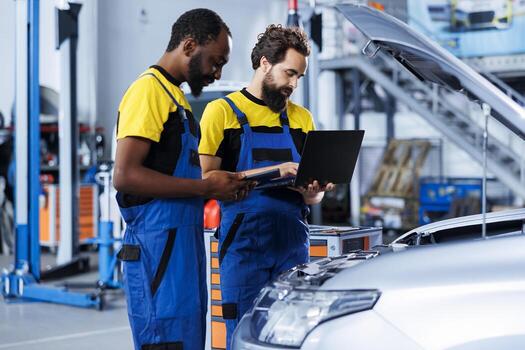 Colleagues in car service using tablet and laptop to calculate repairments invoice for client after fixing engine. Employees using devices to determine final costs after servicing vehicle photo