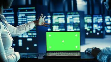 Tech savvy admins running code on chroma key laptop, troubleshooting data center equipment. Specialists using mockup device to monitor servers, networking systems and storage arrays photo