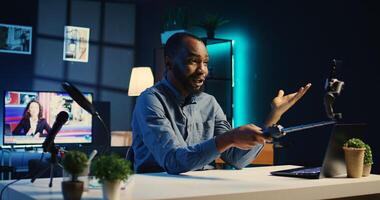 BIPOC content creator using selfie stick smartphone, doing for fans showing his new home studio design. Media star films himself for audience using mobile phone camera, handheld camera shot photo