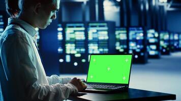Employee using green screen laptop to fix data center hardware clusters providing processing resources for different workloads. Engineer helped by mockup device to repair blade servers photo