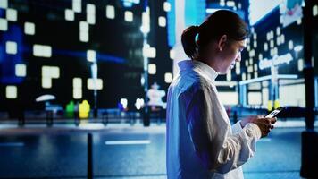 Asian man strolling around city streets at night, using smartphone to do online purchases, looking at products. Carefree person enjoying wandering in empty metropolitan landscape, using mobile phone photo