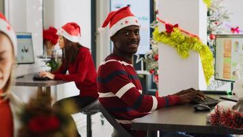 Portrait of friendly african american startup employee checking documents for accuracy in decorated office during Christmas. Workers solving tasks at workstation in multiracial workspace photo