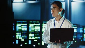 Trained employee strolling through server rows providing processing resources for different workloads. Asian dilligent worker monitoring supercomputers tasked with solving complex operations photo