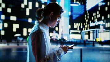 Asian man strolling around cityscape at night, browsing on the internet using smartphone. Businessman walking on the streets at night in empty urban setting using mobile phone photo
