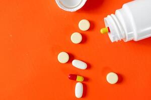 Pills and capsules spilled from a bottle on orange background photo