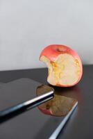 Bitten Apple Next to Smart phone on Reflective Surface photo