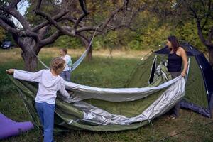 mother and little daughters are setting up a tourist tent in forest, camping with children photo