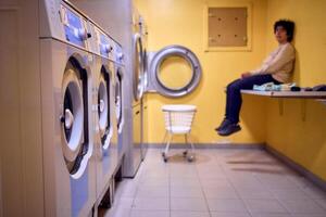 young plus size woman loads clothes into a washing machine in a laundry room in the basement of a student dormitory photo