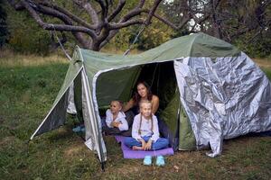mother and little daughters are setting up a tourist tent in forest, camping with children photo