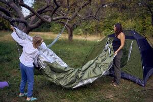 mother and little daughters are setting up a tourist tent in forest, camping with children photo