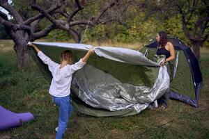 mother and little daughters are setting up a tourist tent in forest, camping with children photo