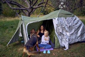 mother and little daughters are setting up a tourist tent in forest, camping with children photo