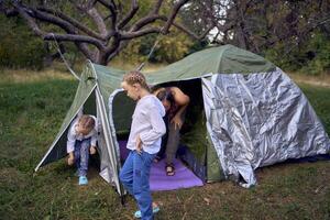 mother and little daughters are setting up a tourist tent in forest, camping with children photo