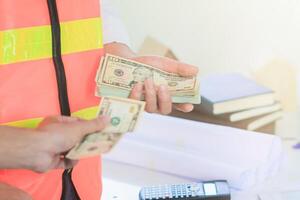 Engineers and Foreman are calculating workers' expenses and overtime to pay workers compensation and overtime each month. Foreman holds cash in hand to pay workers as compensation photo