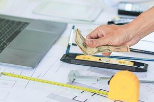 Engineers and Foreman are calculating workers' expenses and overtime to pay workers compensation and overtime each month. Foreman holds cash in hand to pay workers as compensation photo