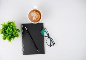 Top view white workspace office desk with office supplies. Flat lay work table with black notebook, Green leaf and coffee cup, Copy space for your advertising content. photo