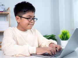Educational of tech concept, Staying at home, Little Asian boy student using computer laptop learning. Presenting a modern educational way of life. Virtual internet online class from school teacher. photo