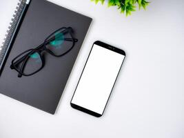 Top view of mock up modern workspace with blank screen smartphone, Coffee cup, Notebook, Pencil, Glasses. Office situation with keyboard and accessories isolated on white. Copy space, Flat lay. photo