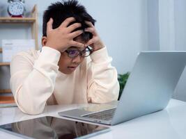 Boy using computer for learning and stressed about online learning, Virtual internet online class from school teacher by remote meeting, Homeschooling and education concept, online education concept. photo
