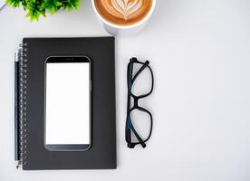Top view of mock up modern workspace with blank screen smartphone, Coffee cup, Notebook, Pencil, Glasses. Office situation with keyboard and accessories isolated on white. Copy space, Flat lay. photo